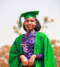 Portrait of a young African woman wearing a green graduation gown and cap, celebrating achievement outdoors.
