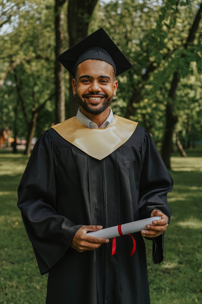 A joyful graduate in cap and gown holding a diploma in an outdoor setting.